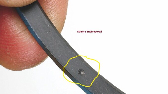 Close-up of a piston ring showing the 'TOP' orientation mark near the end gap.